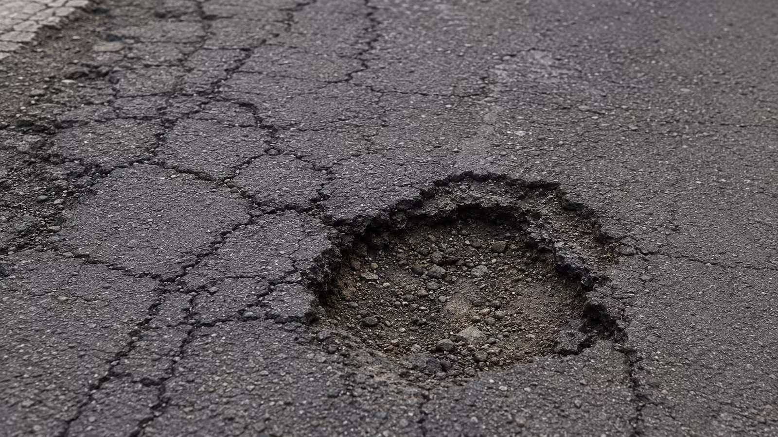 Praskliny a výtluky v poškozeném asfaltovém povrchu